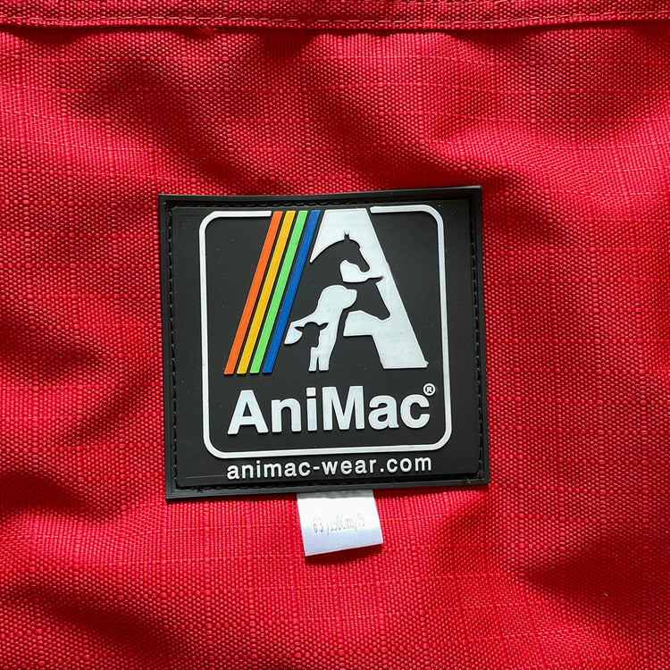 A close-up of red fabric from the Airflow Between Combo Waterproof Lightweight Turnout horse rug, showing a black-and-white AniMac label with a horse, dog, sheep, colorful stripes, and animac-wear.com beneath the logo.