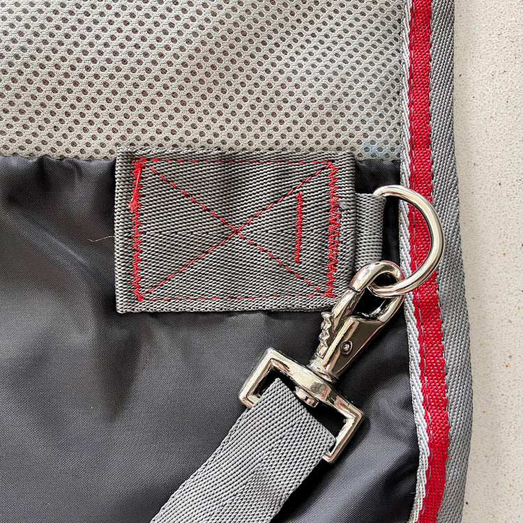 Close-up of a gray fabric strap with metal swivel clip and reinforced red stitching on the Airflow Between Combo | Waterproof Lightweight Turnout, featuring durable gray material and gray-red bordered New Zealand rug design.