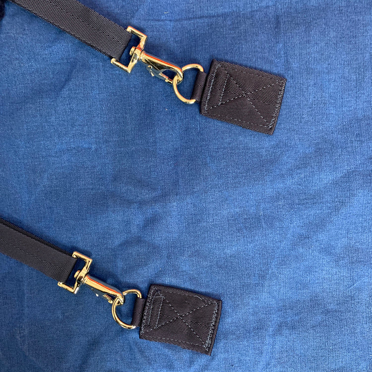 Two black bag straps with gold swivel hooks and leather ends are placed on a blue wool lining of the AniMac Canvas Turnout Rug | New Zealand 18oz Wool Lined Rug, with the hooks attached to fabric loops by visible stitching.